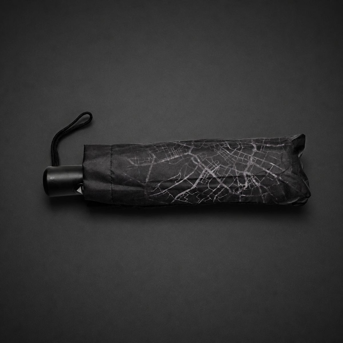 Folded umbrella showing the Manchester map pattern, black handle and wrist strap