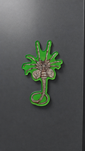 Facehugger-inspired metal fridge magnet with a silver creature wrapped around a circular frame