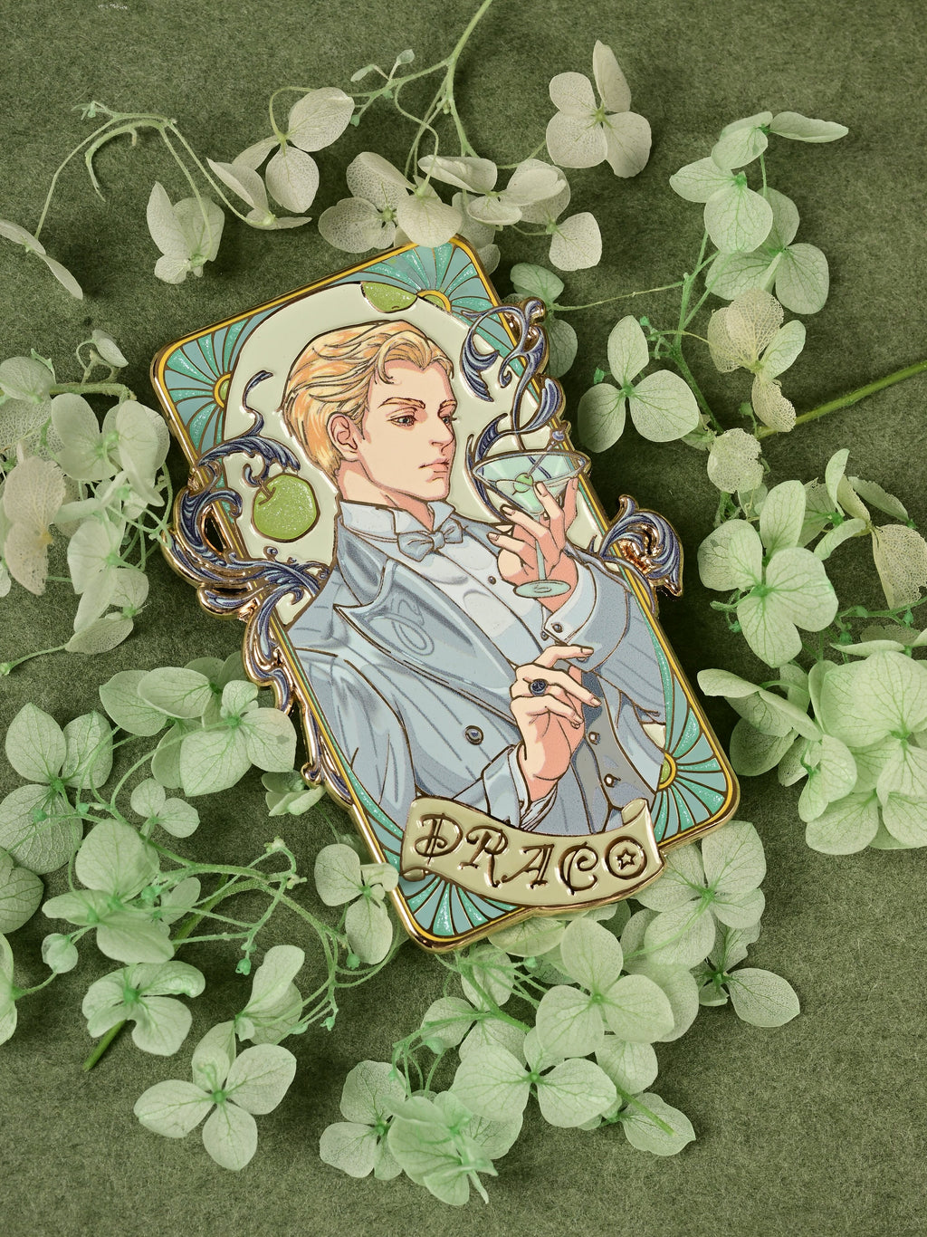 Full view of the Jazz Age 1920 Darco enamel pin arranged among pale green flowers on dark green fabric