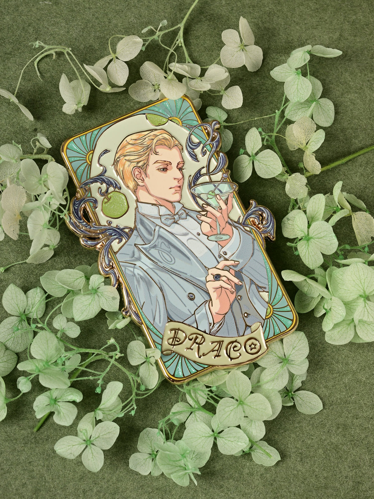 Full view of the Jazz Age 1920 Darco enamel pin arranged among pale green flowers on dark green fabric